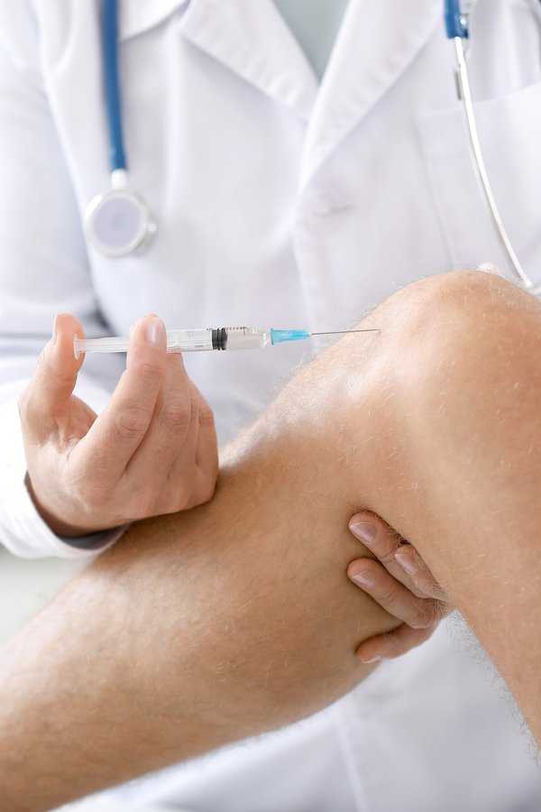 Doctor injecting needle into knee of patient